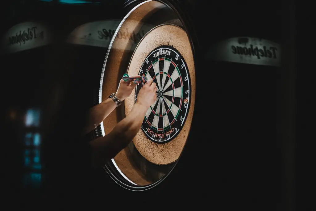 Close up of a person removing darts from a dart board. 