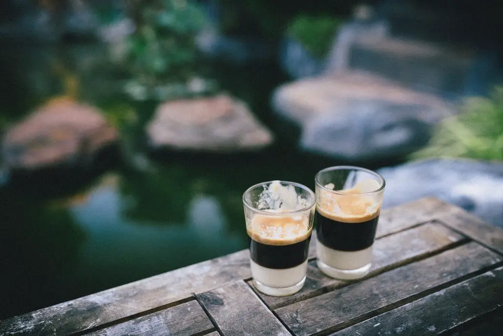Close up of two filled shot glasses next to a lake